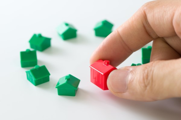 Qué es una inmobiliaria; imagen de una persona colocando pequeñas casas de plástico siendo una de color rojo como símbolo de la función que hacen los agentes inmobiliarios.